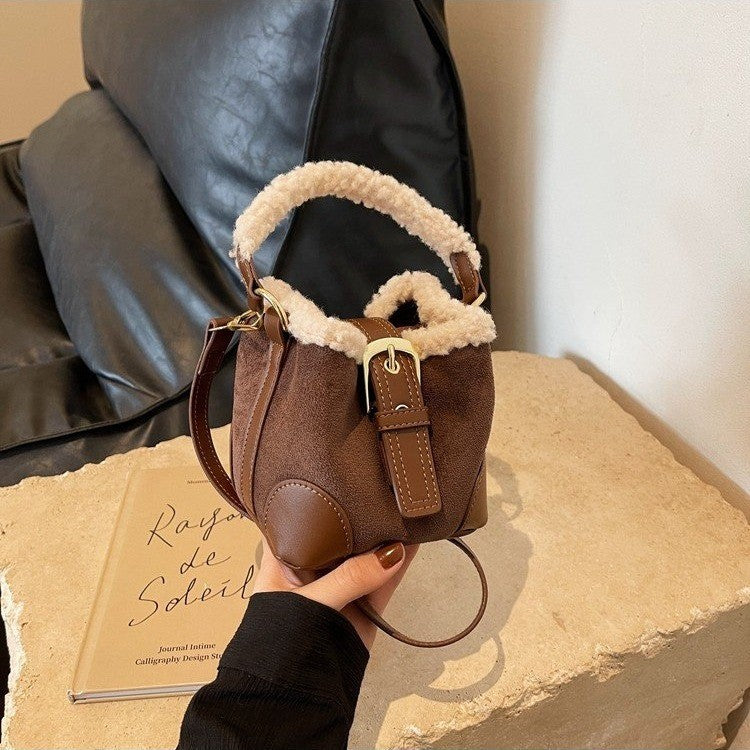 Coffee Plush Agenda Mini Messenger Bag held in hand, front view showing plush trim, top handle, shoulder strap, and buckle tab.