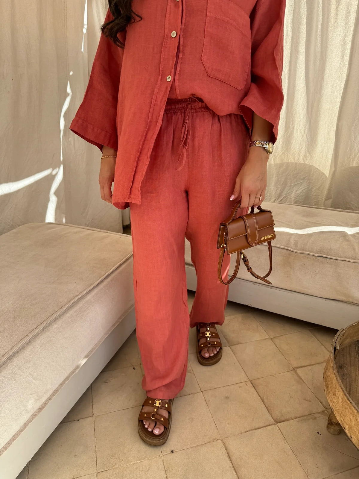 Close front view of the orange-red shirt and elastic-waist trousers with handbag.