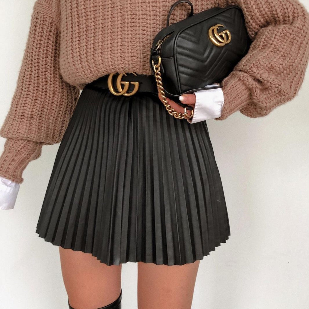 Adult model wearing the black accordion-pleat mini skirt with a brown knit sweater; handbag and belt are styling only.