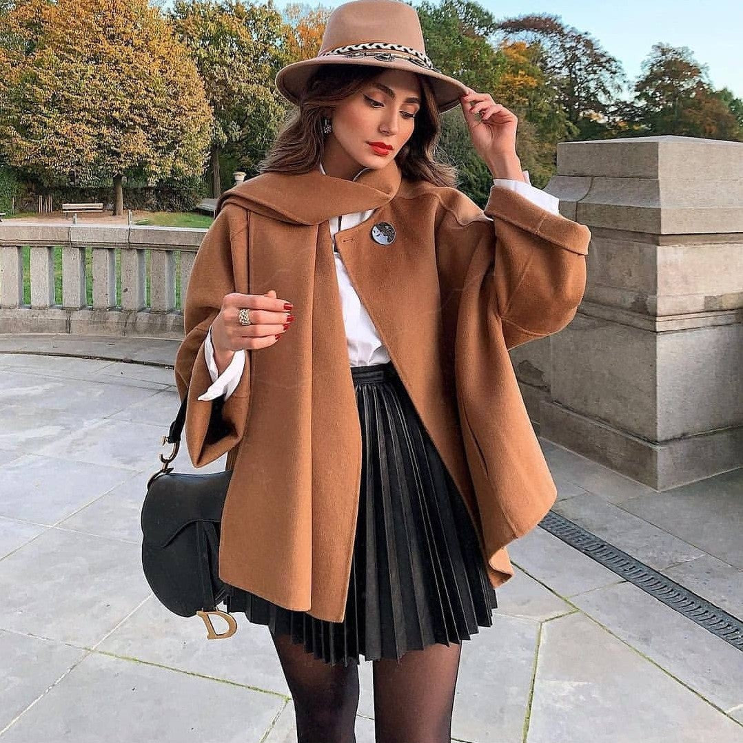 Adult model wearing the black accordion-pleat mini skirt with a camel cape and hat; accessories are styling only.