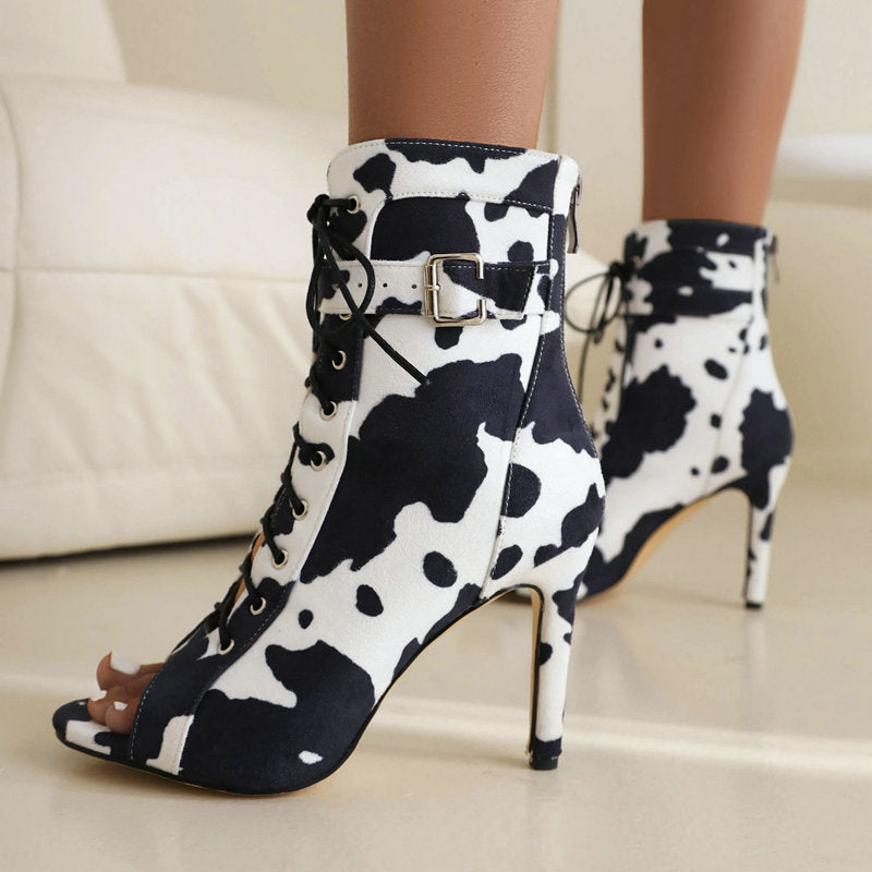 Black-and-white cow-print lace-up open-toe stiletto booties worn as a pair