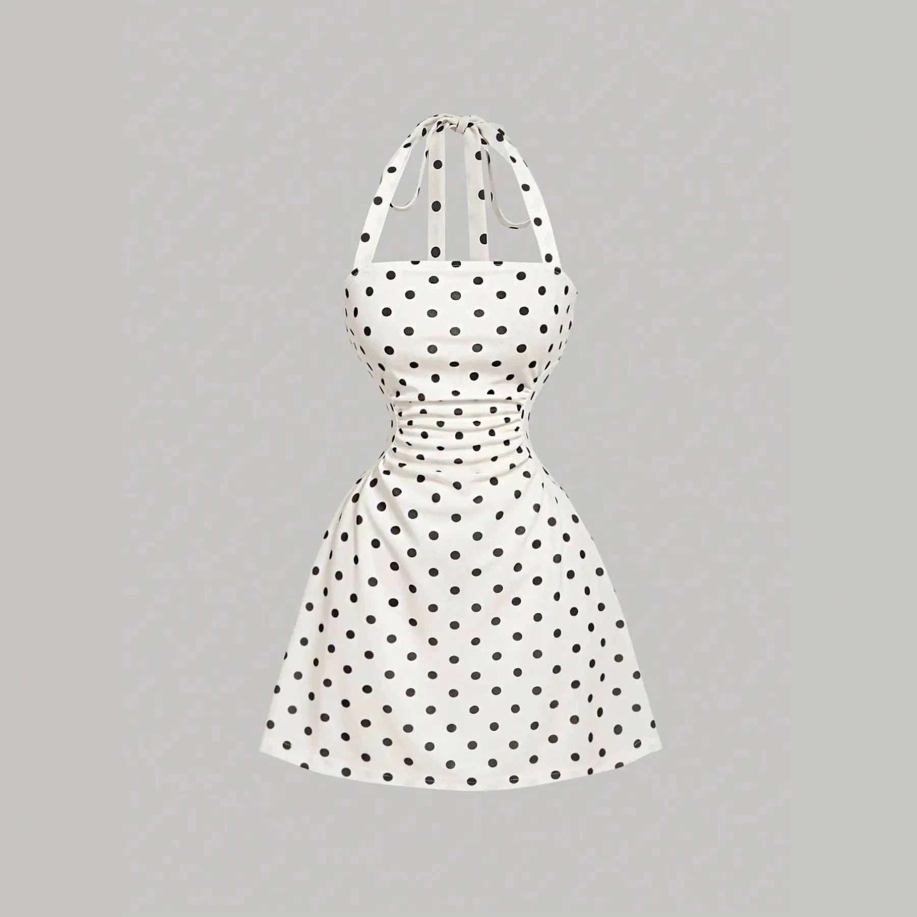White A-line mini dress with black polka dots, ruched waist and tie-back halter straps, front product view.