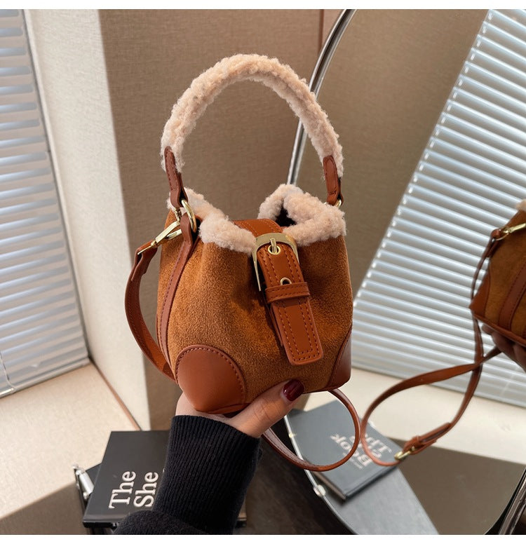 Brown Plush Agenda Mini Messenger Bag held in hand, three-quarter view showing the strap, plush trim, buckle, and stitched corner panel.