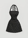 Black A-line mini dress with white polka dots, ruched waist and tie-back halter straps, front product view.