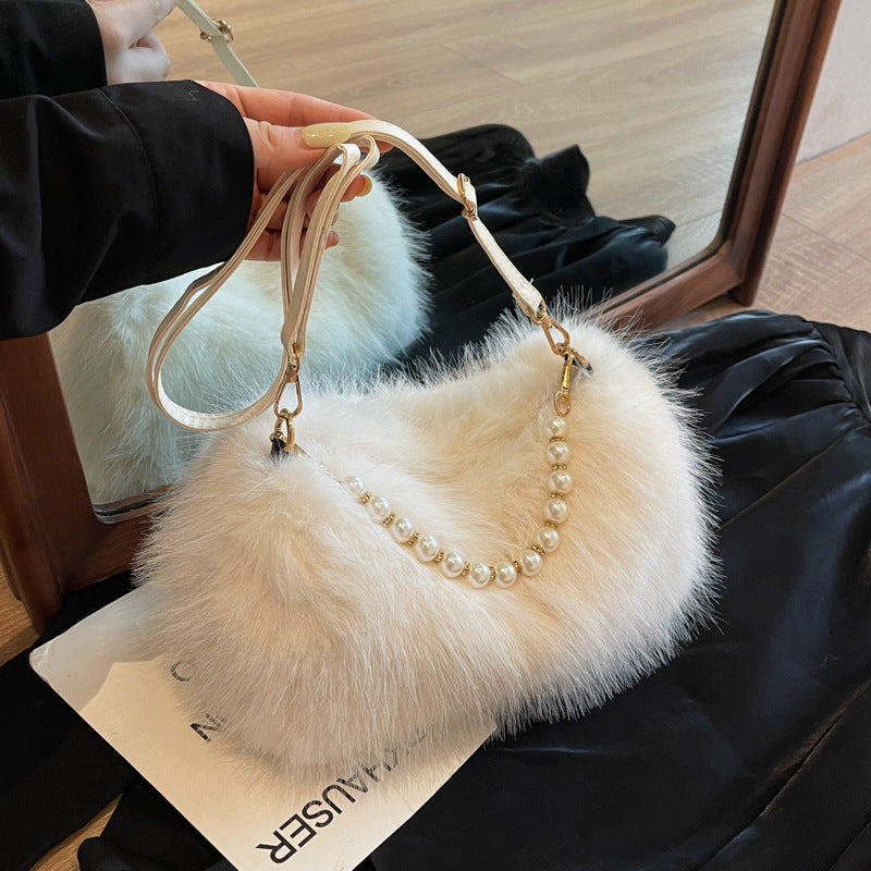 Beige plush shoulder bag with pearl-style front row and adjustable single strap, angled lifestyle view.