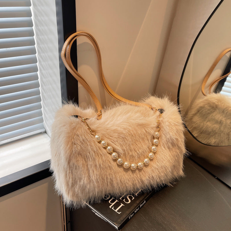 Beige plush shoulder bag with pearl-style front row displayed beside a mirror.