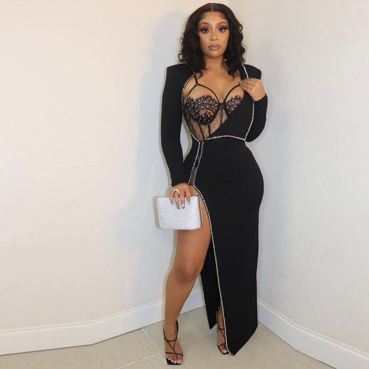 Model wearing the black Billion Moves Maxi Dress with long sleeves, jeweled sheer bodice, rhinestone trim, high thigh slit, and silver clutch.