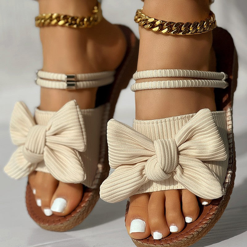 Bow & Gold Vacation Sandals supplier reference view 1 showing apricot and black flat bow sandals with ankle-wrap cords, stitched soles and gold chain details