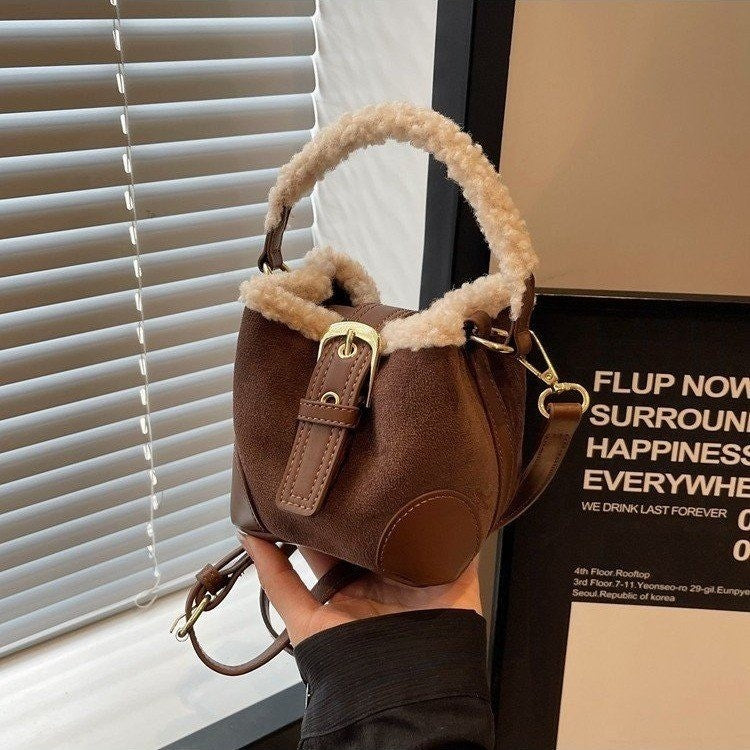 Brown Plush Agenda Mini Messenger Bag held in hand, showing the plush-trimmed handle and opening, shoulder strap, and buckle tab.