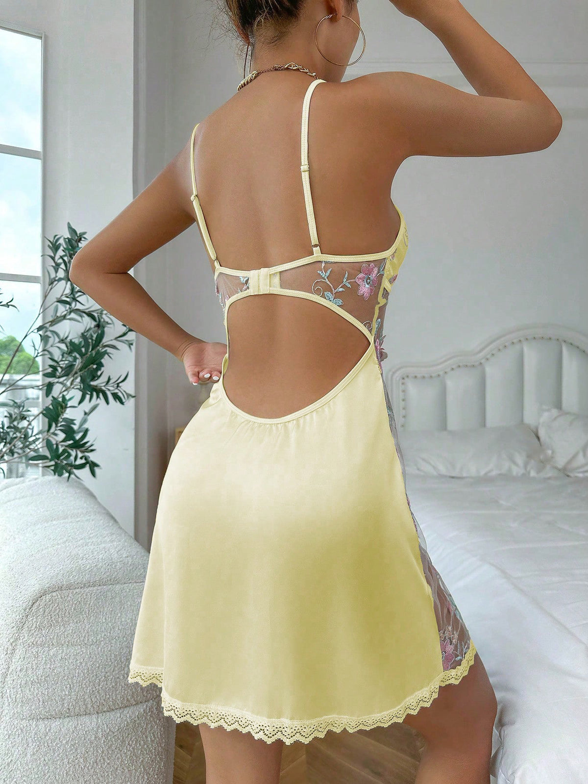 Back view of the yellow satin-look mini slip showing slim straps, floral mesh and open-back cutout.