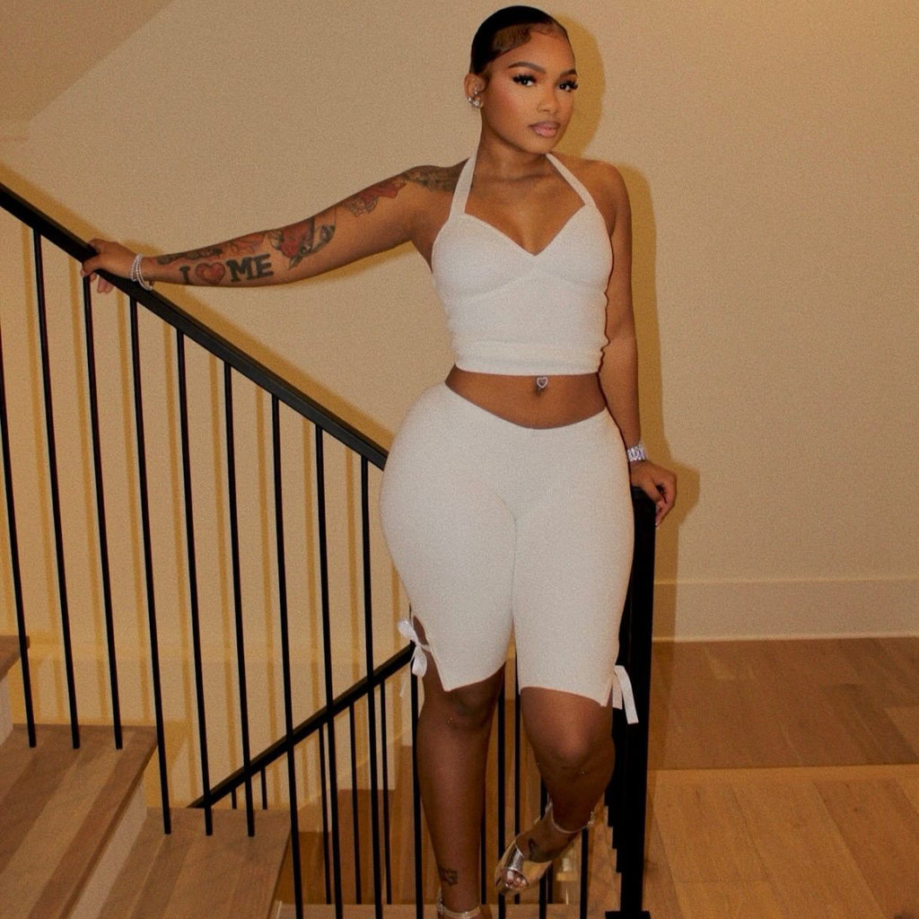 Model wearing a white halter crop top and white side-tie cropped pants by a staircase.