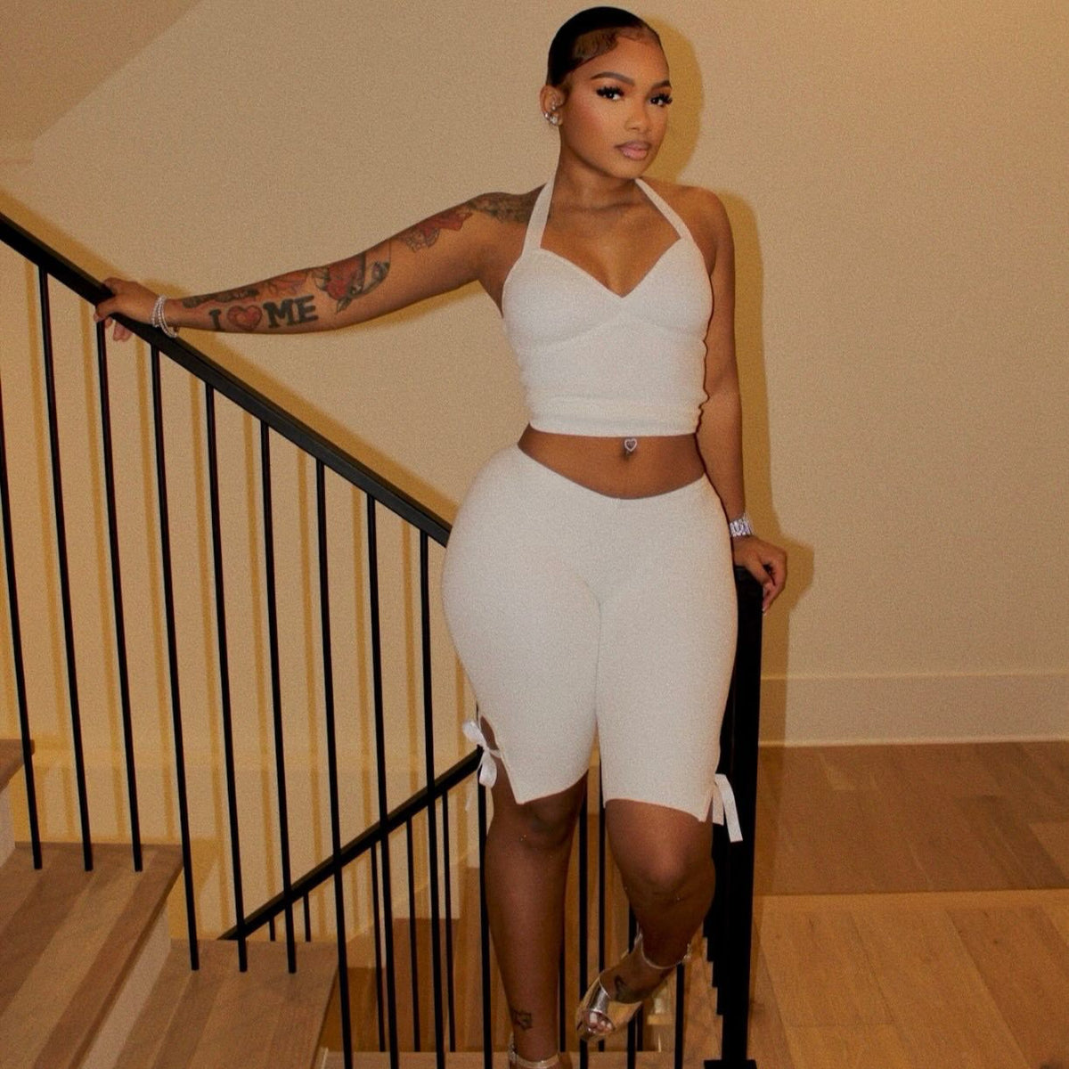 Model wearing a white halter crop top and white side-tie cropped pants by a staircase.