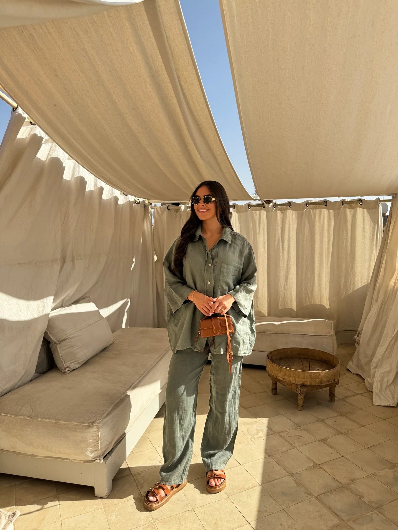 Full-length view of an adult model wearing the army-green shirt and wide-leg trouser set on a shaded patio.