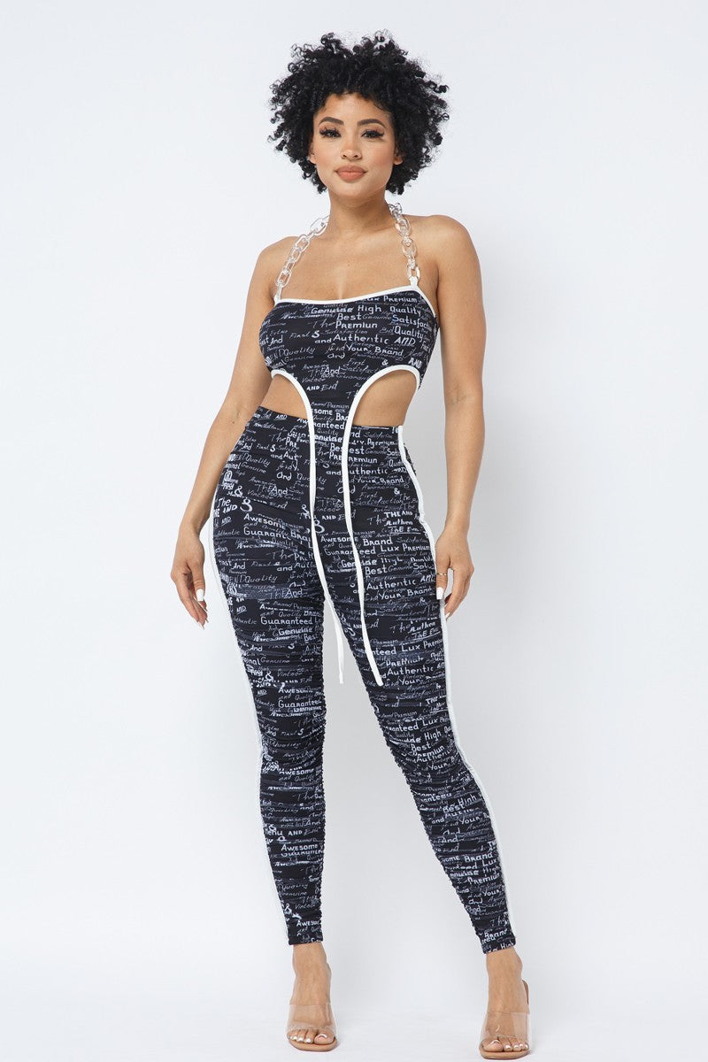 Adult model wearing the black-and-white handwritten-print chain-halter crop top with matching ruched leggings, full front view