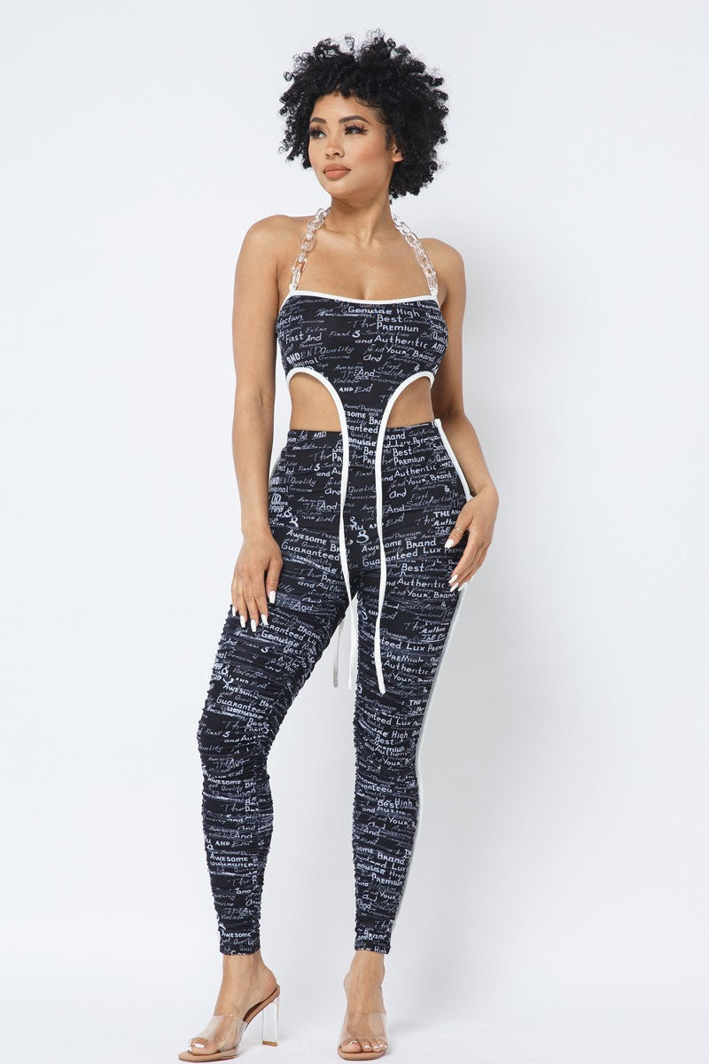 Black-and-white printed chain-halter crop top with white-piped side cutouts and matching ruched leggings, front view