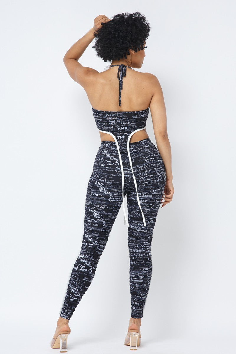 Rear view of the black-and-white printed set showing the halter tie, open crop-top back, long white-edged ties and ruched leggings