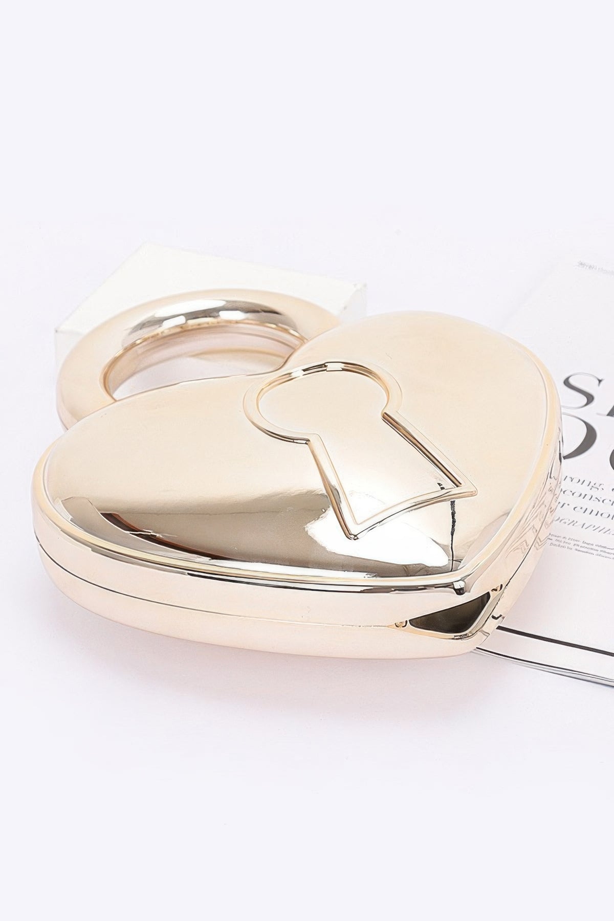 Gold heart-shaped Metallic Acrylic Bag lying flat to show rigid case depth, handle and keyhole motif