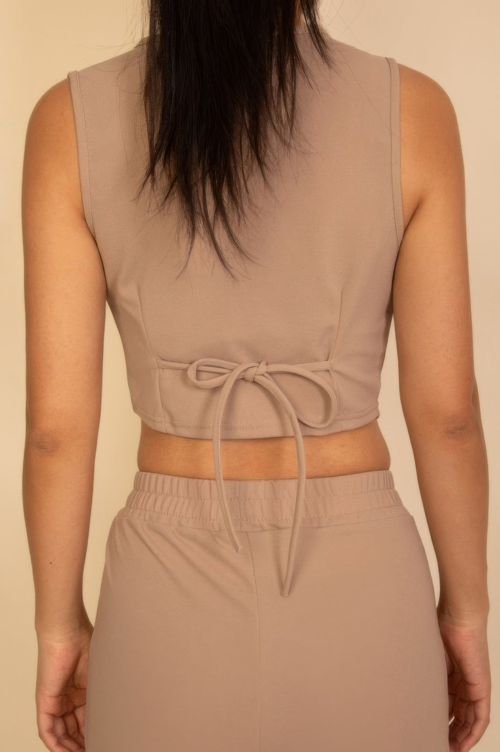 Close rear view of the taupe vest adjustable bow tie above the pants elastic waistband