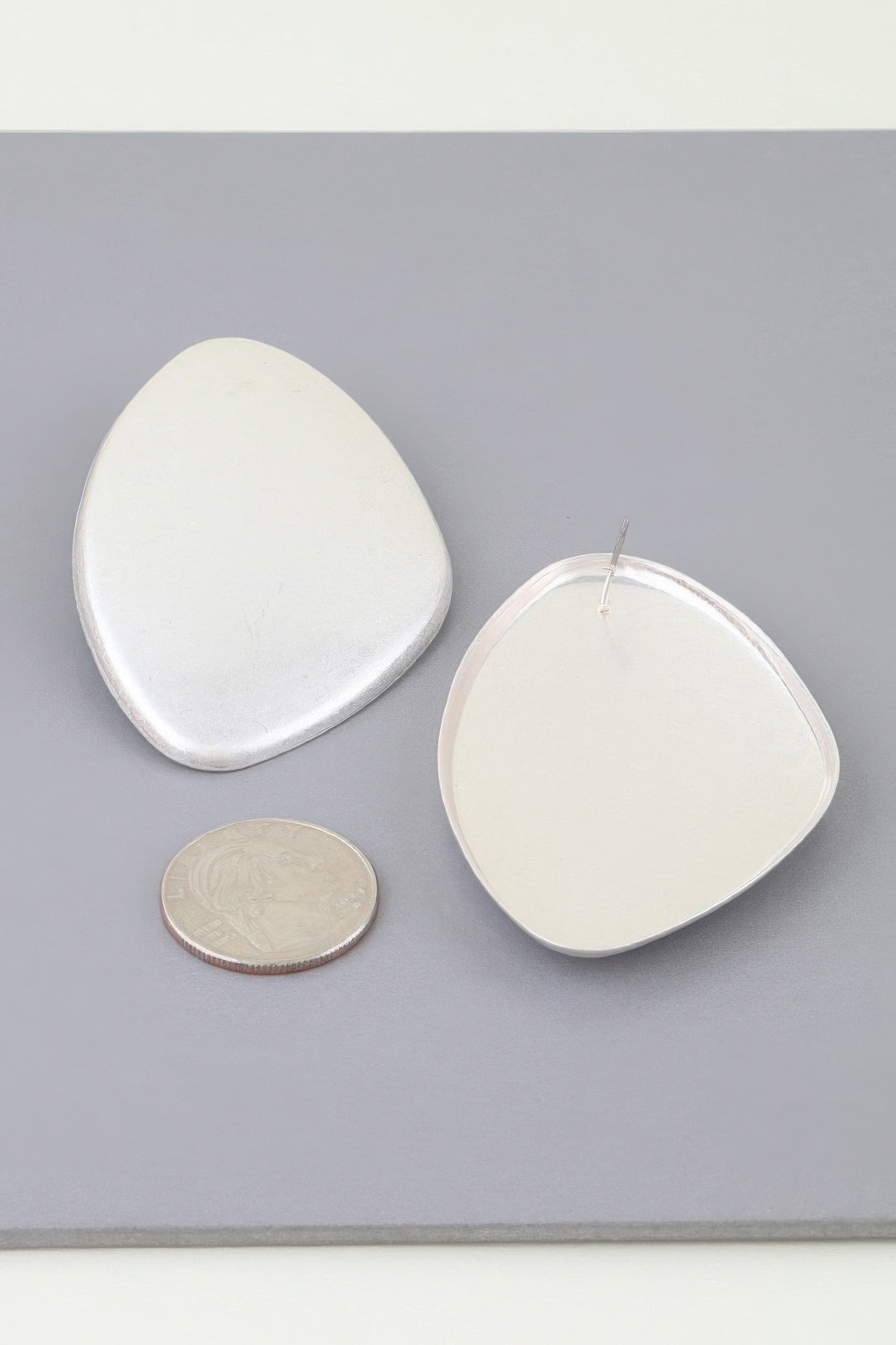 Silver-tone Power Plate earrings shown beside a coin for scale