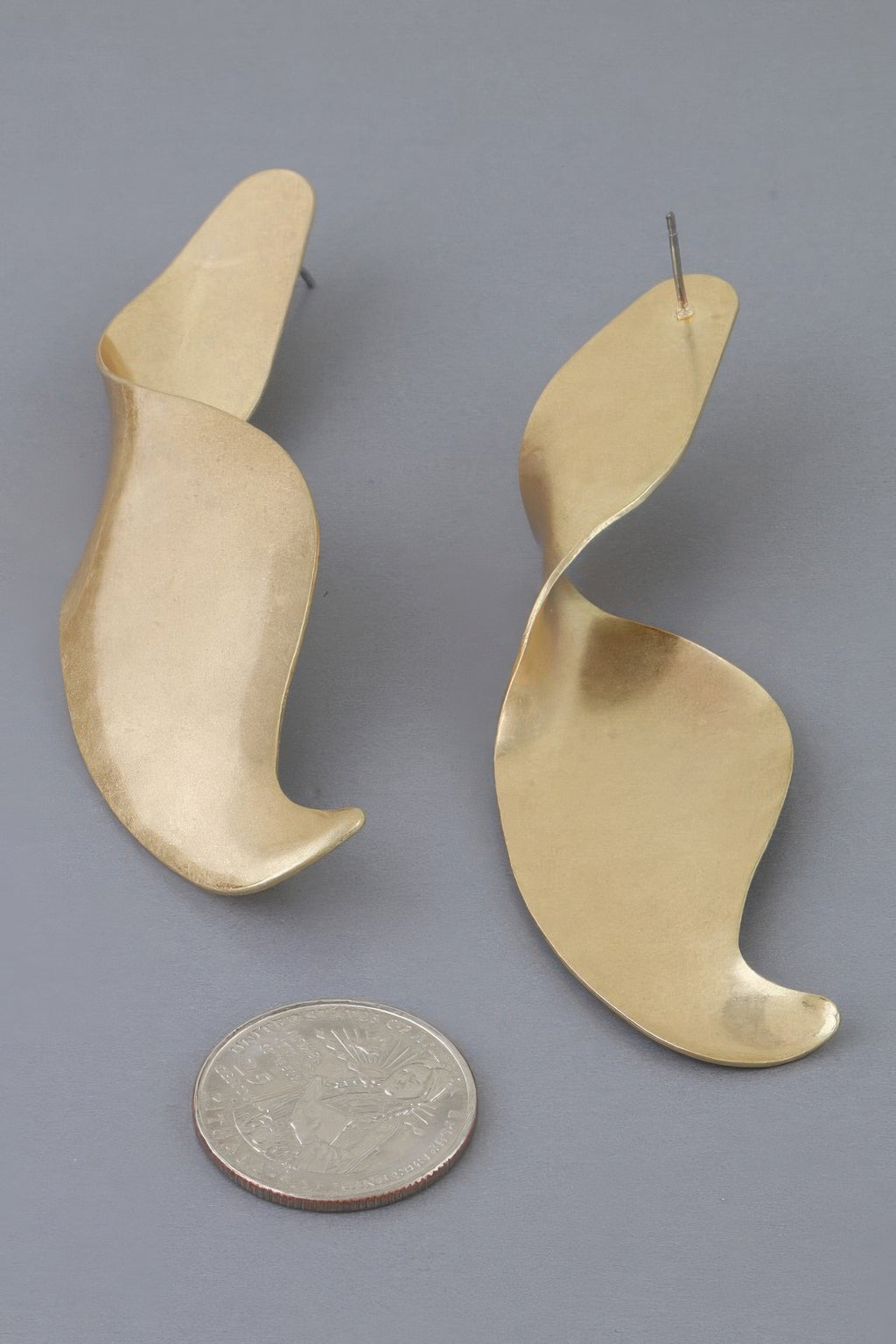 Gold-tone Liquid Motion swirl earrings shown beside a coin for scale
