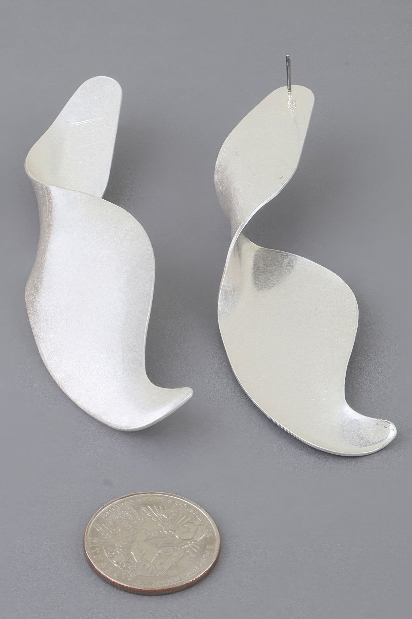Silver-tone Liquid Motion swirl earrings shown beside a coin for scale