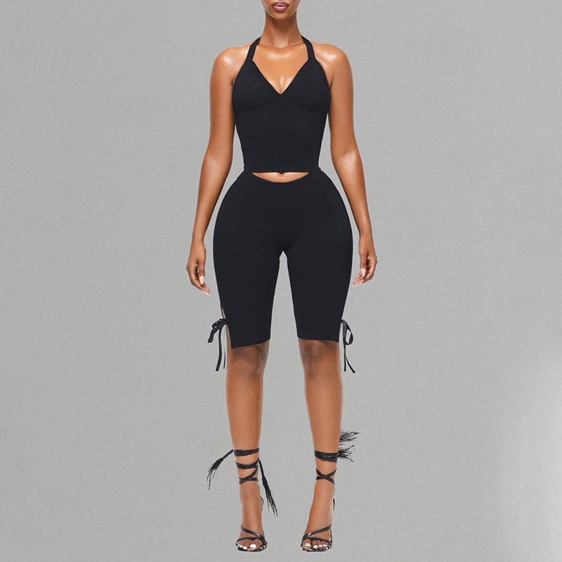 Front view of a black halter crop top and black side-tie cropped pants on a gray background.
