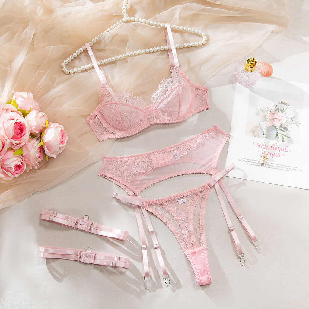 Pink lace four-piece lingerie set arranged flat with bra, panties, camisole garter piece, and straps.