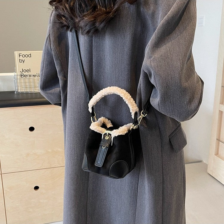 Black Plush Agenda Mini Messenger Bag worn over the shoulder against a gray coat, rear lifestyle view.