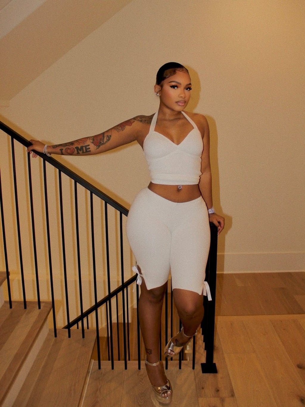 Full-length view of a model wearing a white halter crop top and white side-tie cropped pants by a staircase.