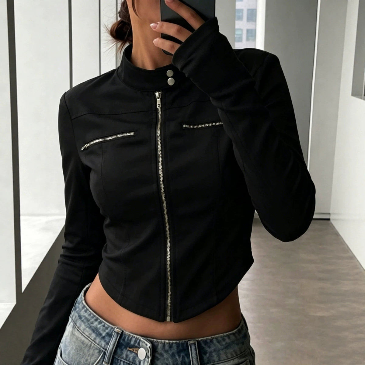 Mirror view of an adult model wearing the black cropped jacket zipped closed with blue jeans.