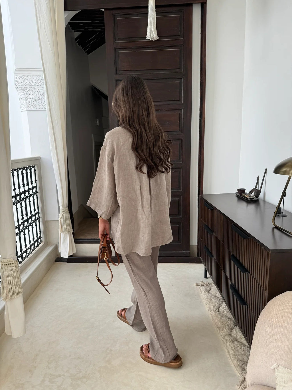 Rear view of an adult model wearing the beige relaxed shirt and wide-leg trousers indoors.