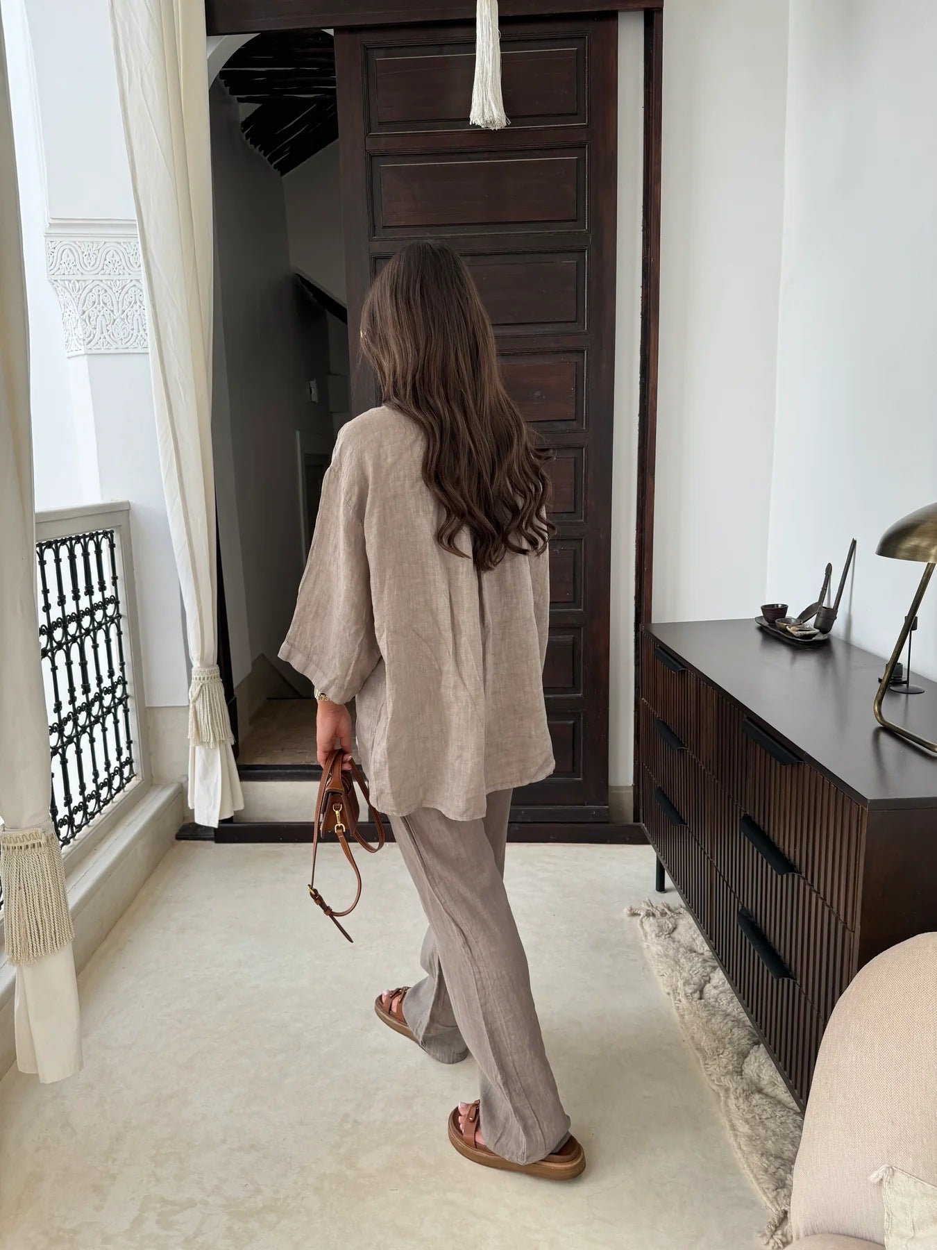 Rear view of an adult model wearing the beige relaxed shirt and wide-leg trousers indoors.