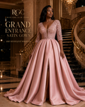 Grand Entrance Satin Gown in dusty pink on an adult model in a luxury hotel, showing the beaded plunge bodice, three-quarter sleeves, box-pleated full skirt, and front slit.