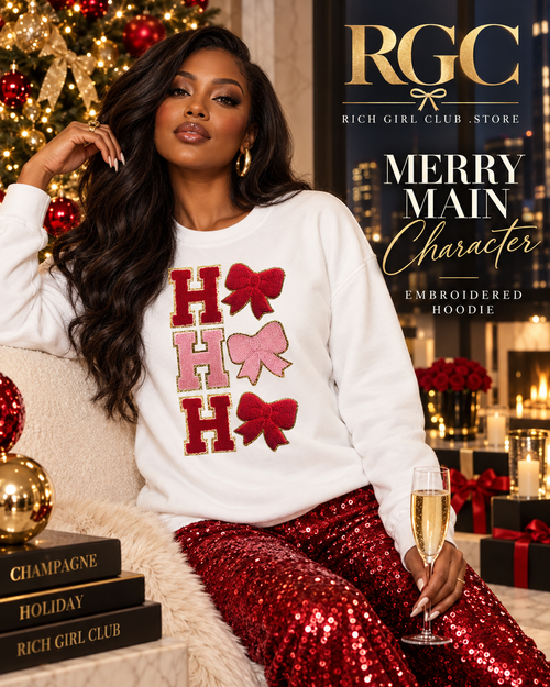Confident adult model wearing the Merry Main Character Embroidered Hoodie in a luxury Christmas penthouse campaign.