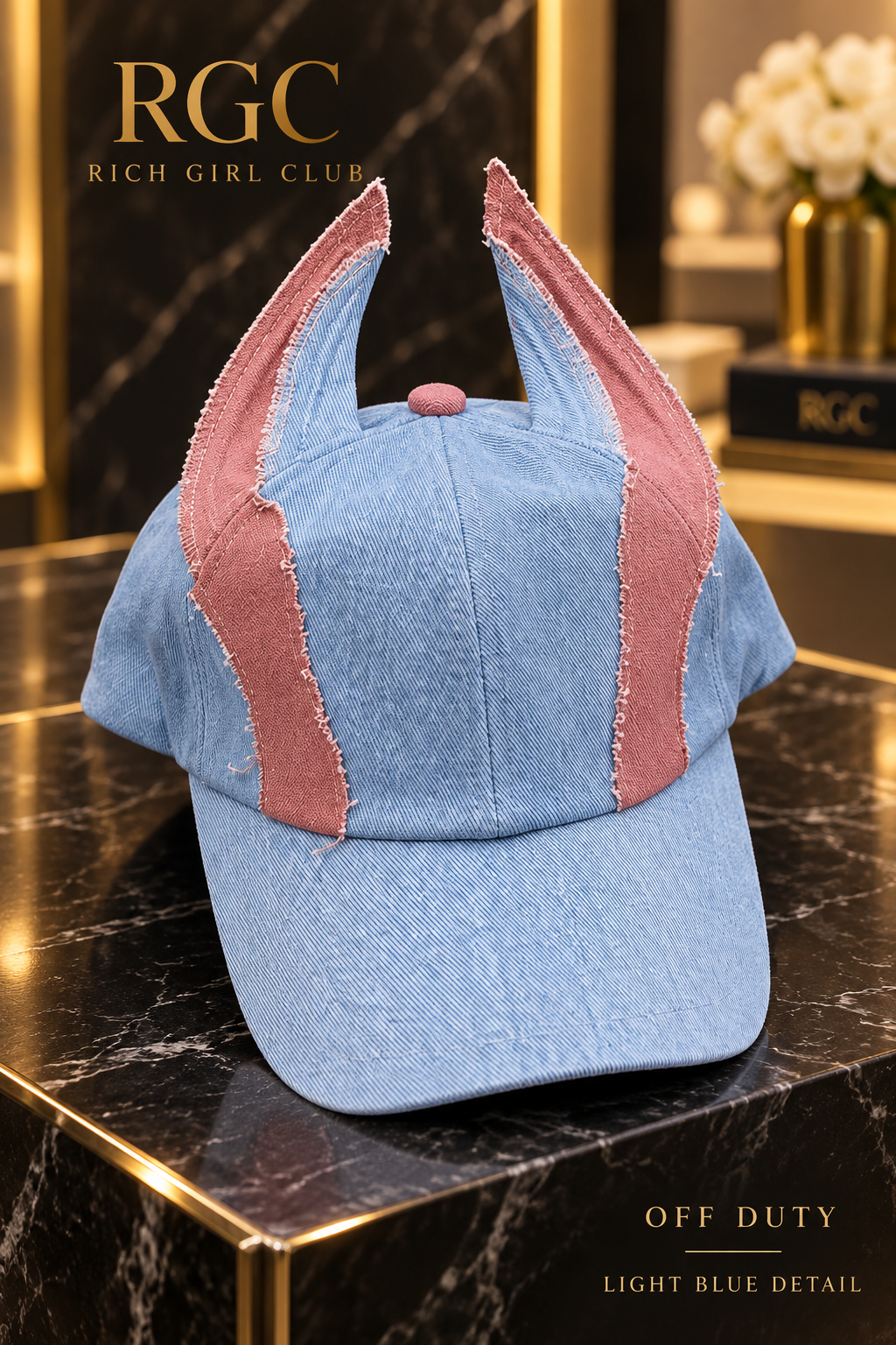 Off Duty Light Blue denim cap by Rich Girl Club shown in detail with a pale blue crown, dusty-pink ear panels, a pink crown button, a curved brim, and raw edges.